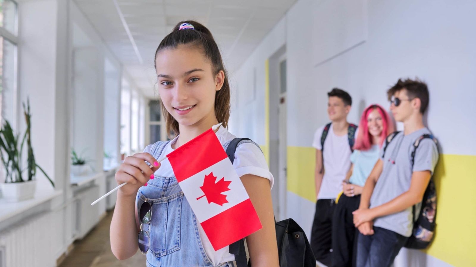 Student teenager female with flag of Canada inside school, children group background. Canada, education and youth, patriotism, people concept
